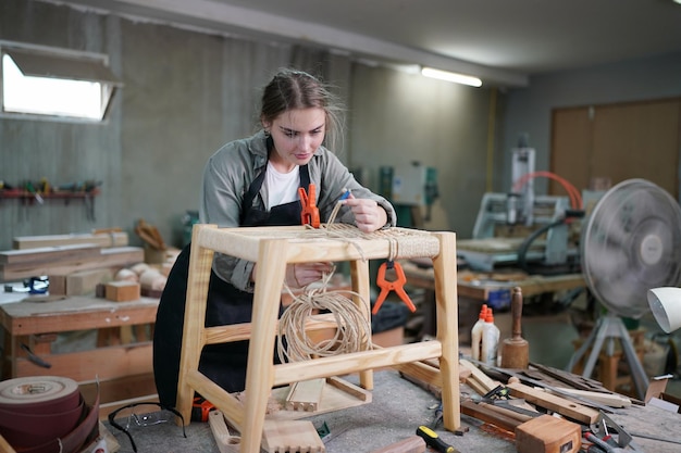 Jonge mooie vrouw doet werk in de timmerman DIY workshopruimte. Eigenaar van een klein bedrijf, jonge vrouw die bij een meubelfabriek werkt.