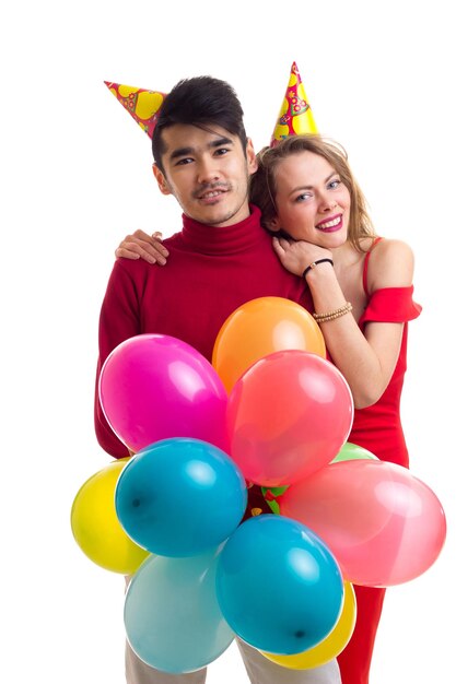 Jonge mooie vrouw en jonge knappe man met het vieren van hoeden met veel gekleurde ballonnen