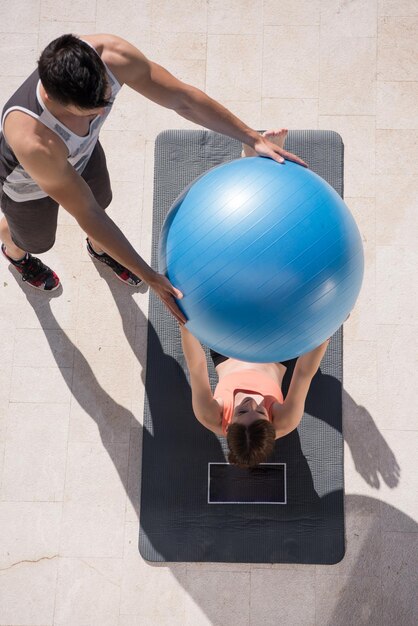 jonge mooie vrouw en personal trainer doen oefening met pilates bal voor haar luxe huis