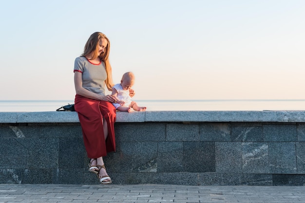 Jonge mooie vrouw en peuter zittend op de promenade op zee achtergrond Vakantie met baby