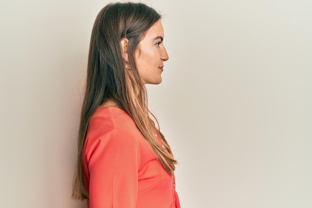 Jonge, mooie vrouw, gekleed in vrijetijdskleding die naar de zijkant kijkt, ontspannen profiel pose met een natuurlijk gezicht met een zelfverzekerde glimlach