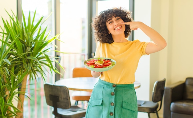 Jonge mooie vrouw glimlachend vol vertrouwen wijzend op eigen brede glimlach, positieve, ontspannen, tevreden houding