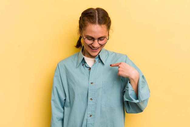 Jonge mooie vrouw glimlachend vrolijk en nonchalant naar beneden kijkend en wijzend naar de borst