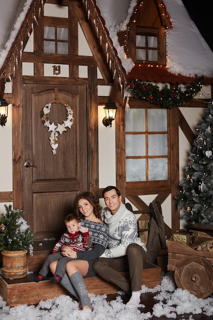 Jonge mooie vrouw, haar knappe echtgenoot en hun schattige zoontje poseren op de trappen van het versierde huis voor Kerstmis