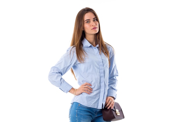 Jonge mooie vrouw in blauw shirt en spijkerbroek met kleine bruine tas met hand op haar taille