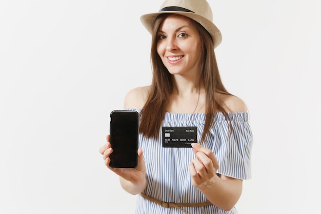 Jonge mooie vrouw in blauwe jurk, hoed weergegeven: camera mobiele telefoon met leeg zwart leeg scherm, met creditcard geïsoleerd op een witte achtergrond. Mensen, bankconcept. Reclame gebied. Ruimte kopiëren