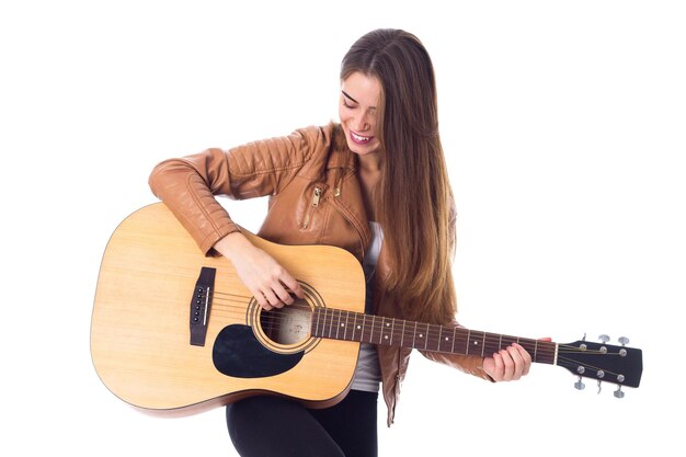 Jonge mooie vrouw in bruine jas en zwarte broek die een gitaar vasthoudt en haar haar repareert