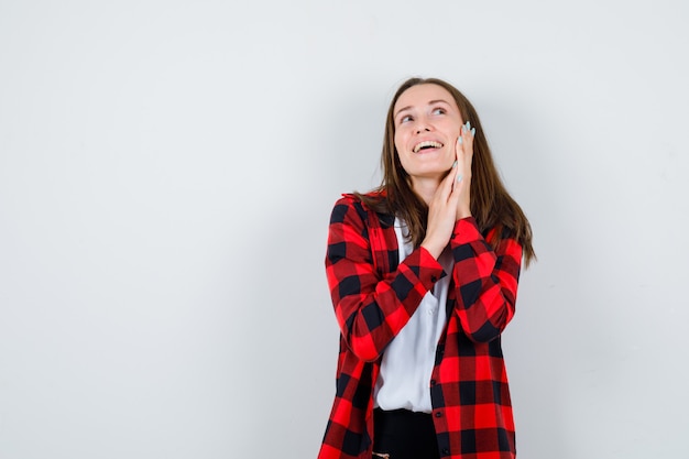 Jonge mooie vrouw in casual outfit met de hand op de wang, wegkijkend en vrolijk kijkend, vooraanzicht.