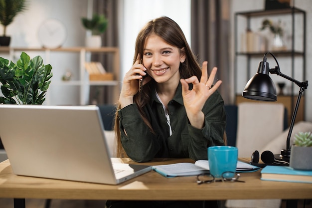 Jonge mooie vrouw in casual outfit praten op mobiele telefoon en typen op laptop