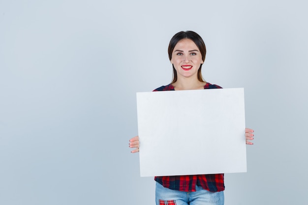 Jonge mooie vrouw in casual shirt met leeg bord en vrolijk, vooraanzicht.