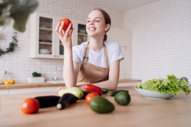 Jonge mooie vrouw in de keuken in een schort en verse groenten op tafel