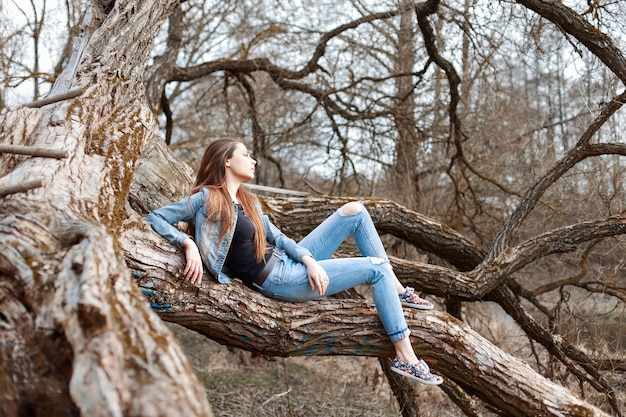 Jonge mooie vrouw in denimkleren die en op een grote boom zitten rusten
