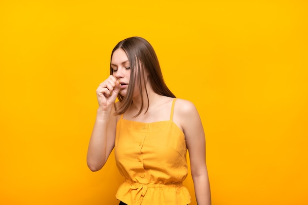 Jonge mooie vrouw in een gele trui hoest in een vuist op een geel