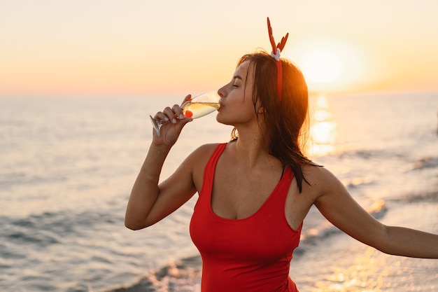 Jonge mooie vrouw in een kerstmuts met een glas champagne in haar handen lopen op het strand