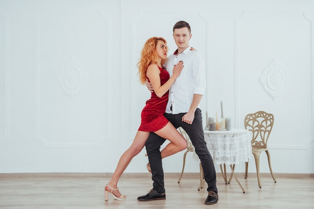 Jonge mooie vrouw in een rode kleding en man dansen geïsoleerd op een witte achtergrond.