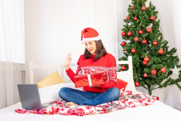 Jonge mooie vrouw in een rode trui en een hoed met geschenken in de buurt van de kerstboom