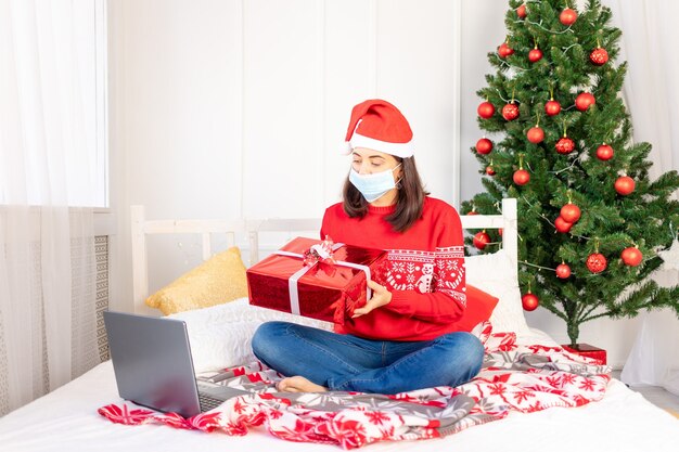 Jonge mooie vrouw in een rode trui en een hoed met geschenken in de buurt van de kerstboom