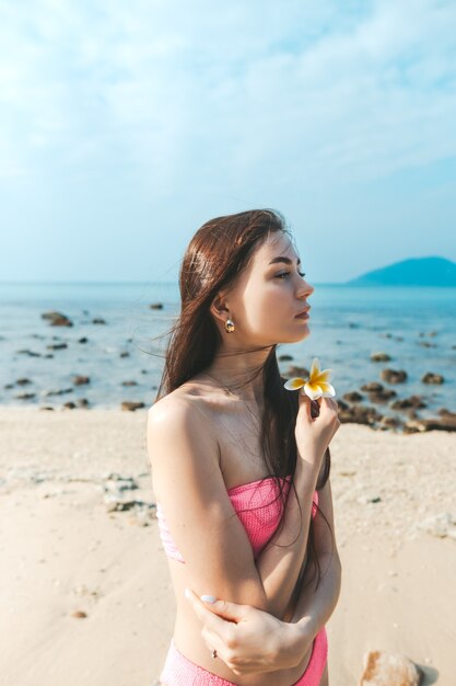 Jonge mooie vrouw in een roze badpak staat op een zandstrand