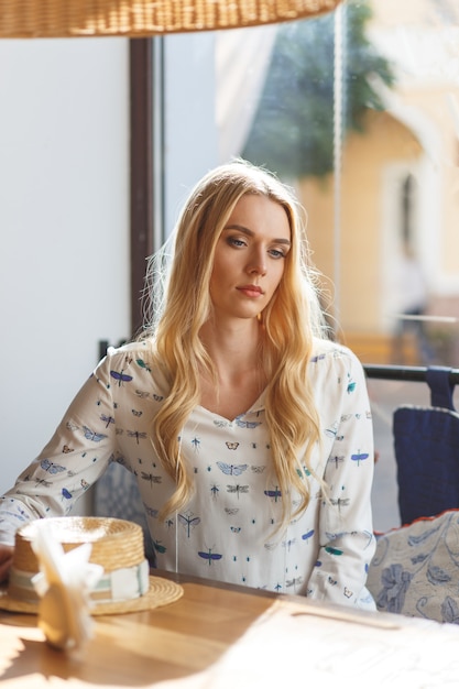 Jonge mooie vrouw in een witte jurk die in café rust