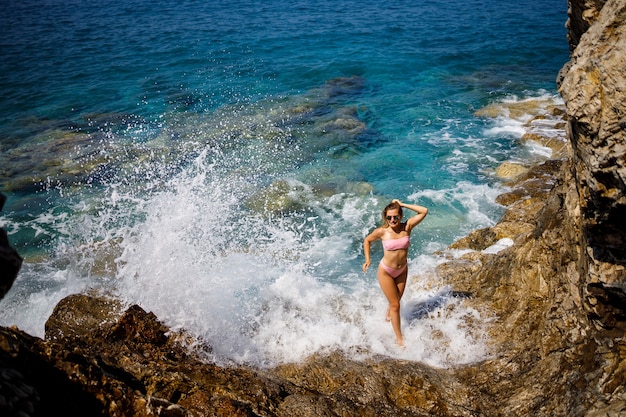 Jonge mooie vrouw in een zwembroek staat op een rotsachtig strand van de Middellandse Zee. Het concept van zeerecreatie. Selectieve focus