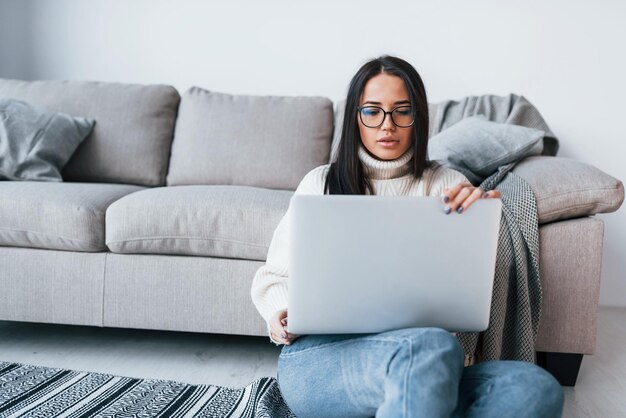 Jonge mooie vrouw in glazen om alleen thuis te zitten met laptop.