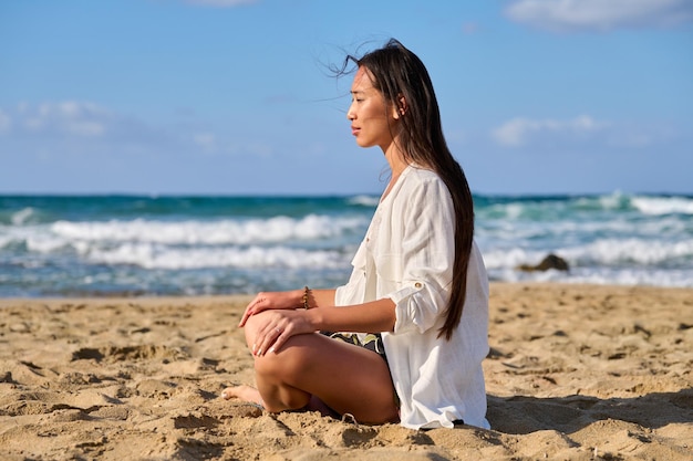 Jonge mooie vrouw in lotuspositie mediteren op het strand