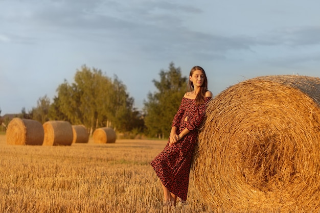 Jonge mooie vrouw in rode jurk close-up op de achtergrond van het veld met hooibergen bij zonsondergang.