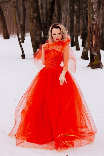 Foto jonge mooie vrouw in rode lange jurk in de sneeuw