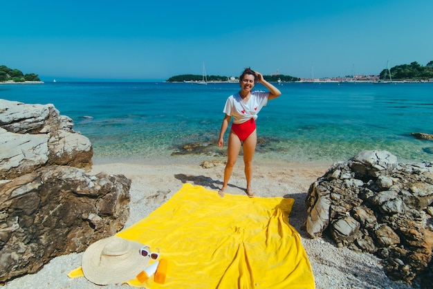 Jonge mooie vrouw in rode zwembroek en witte t-shirt op strand blauw helder zeewater op background