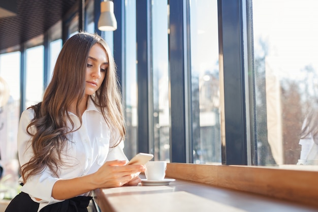 Jonge mooie vrouw in smartphone van het bedrijfsklerengebruik in een koffie