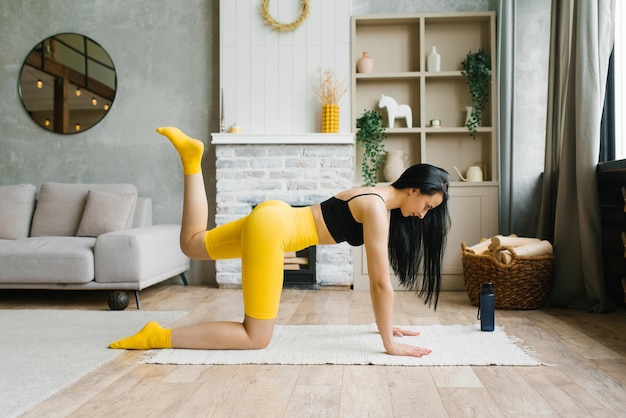 Jonge mooie vrouw in sportkleding doet thuis een fitnesstraining en tilt haar benen op