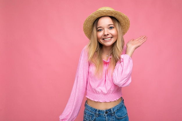 Jonge mooie vrouw in stijlvolle roze zomerblouse en trendy strohoed positieve vrouwelijke shows