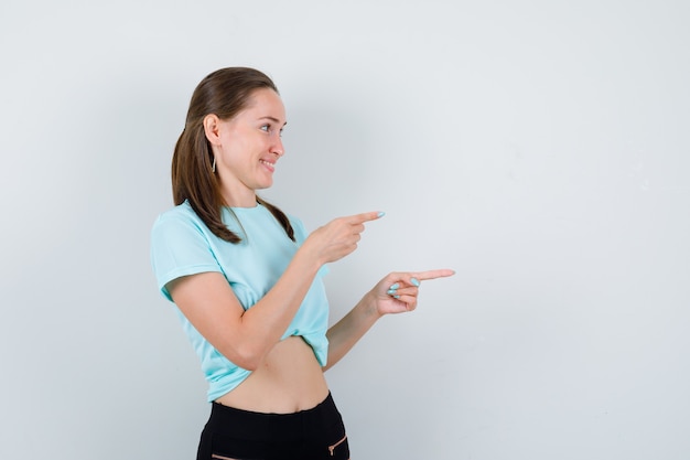 Jonge mooie vrouw in t-shirt naar rechts wijzend, opzij kijkend en gelukzalig kijkend, vooraanzicht.