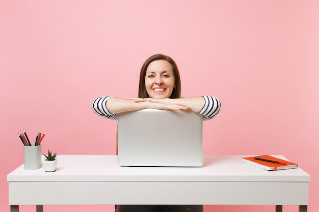 Jonge mooie vrouw in vrijetijdskleding die aan een project werkt, leunend op een laptop terwijl ze op kantoor zit