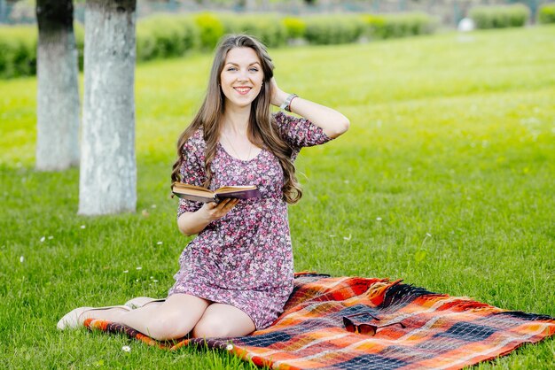 Jonge mooie vrouw in zomerjurk ontspannen en lezen van een boek in het park