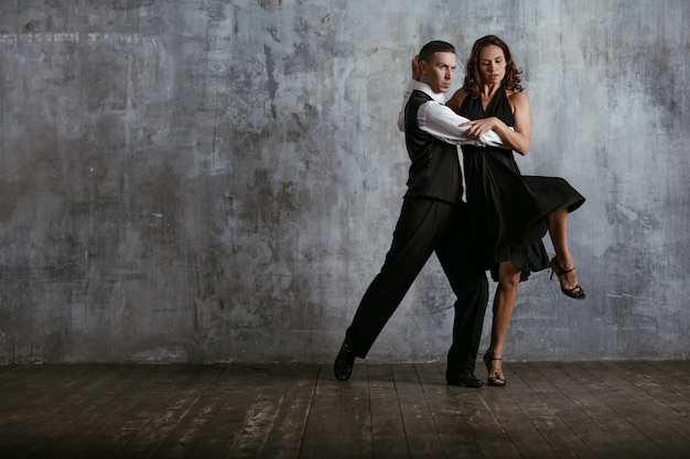 Jonge mooie vrouw in zwarte jurk en man tango dansen