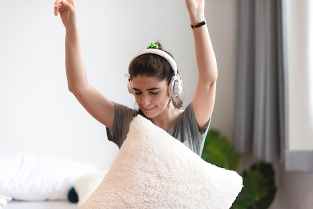 Jonge, mooie vrouw is gelukkig en geniet van muziek door een oortelefoon te gebruiken om thuis een geluid te luisteren in de slaapkamer, ontspannen en leuke levensstijl met een liedmelodie house entertainment headset-concept