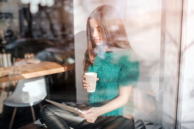 Jonge mooie vrouw koffie drinken in café-bar. Vrouwelijk model Young met behulp van digitale tablet in café