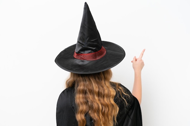 Jonge mooie vrouw kostuum als heks geïsoleerd op een witte achtergrond die terug wijst met de wijsvinger
