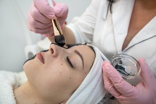 Jonge mooie vrouw krijgt een zwart cosmetisch gezichtsmasker in de schoonheidssalon