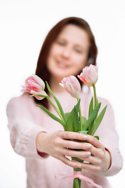 Jonge mooie vrouw lichte trui geeft roze tulpen op witte achtergrond. Vervagen portret, selectieve focus.