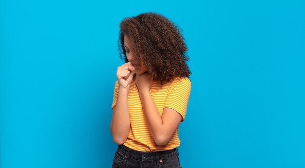 jonge mooie vrouw met afrohaar en geel shirt poseren op blauwe muur