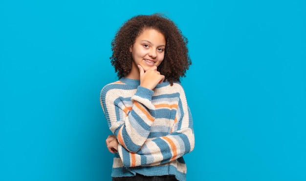 jonge mooie vrouw met afrohaar en gestreepte trui die zich voordeed op blauwe muur