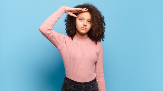 jonge mooie vrouw met afrohaar en roze trui die zich voordeed op blauwe muur