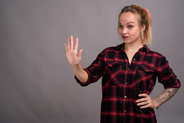 jonge mooie vrouw met blond haar, gekleed in rood geruit overhemd op grijs