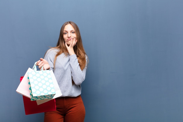 Jonge mooie vrouw met boodschappentassen tegen blauwe muur met een kopie ruimte