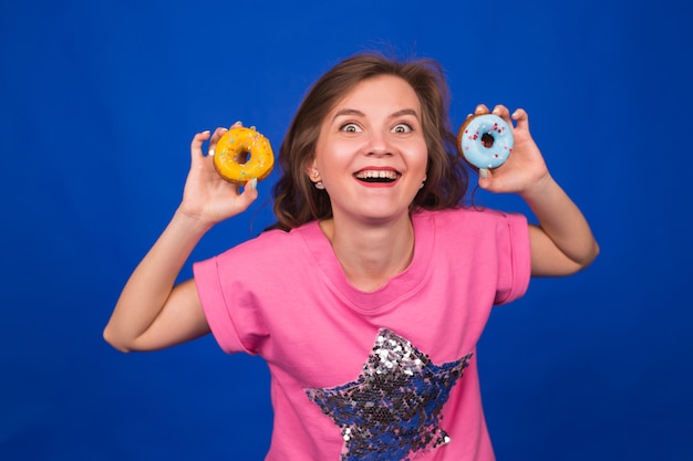 Jonge mooie vrouw met donut op blauw