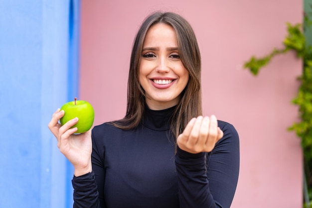 Jonge mooie vrouw met een appel in de open lucht die uitnodigt om met de hand te komen Blij dat je gekomen bent