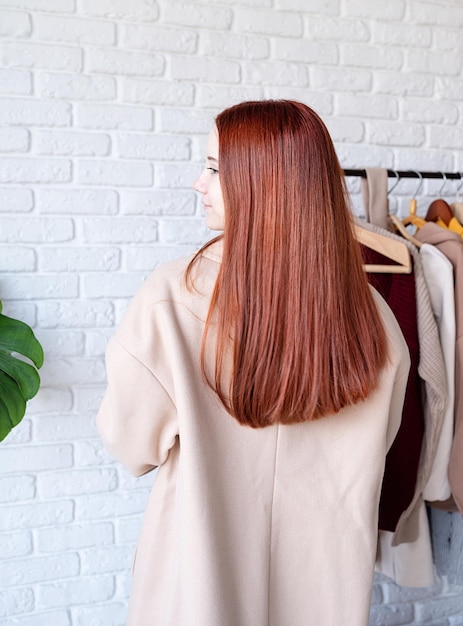 Jonge, mooie vrouw met een beige pastelkleurige jas die in de buurt van kledingrekken staat