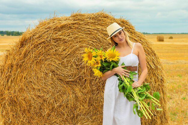Jonge mooie vrouw met een boeket zonnebloemen in een veld in de buurt van een hooiberg